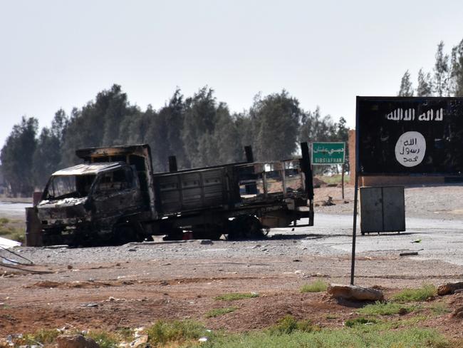 A general view shows a burnt out vehicle next to a banner bearing the Islamic State group's flag in the village of Dibsiafnan on the western outskirts of Raqa.  Picture:  AFP