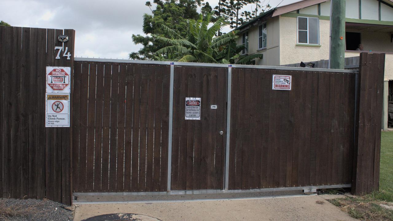 The property is bounded by a high wooden fence topped with spikes, displaying signs warning of video surveillance.