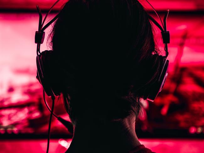 Woman wearing headphones playing video games late at night. Video games, gaming, screen time, kids and technology, headphones, generic