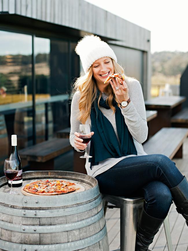 A vistor enjoys one of Devil’s Corner’s award-winning wines with a slice of wood-fired pizza on the deck at the stunning East Coast winery’s cellar door. Picture: Tourism Tasmania/Lisa Kuilenburg.