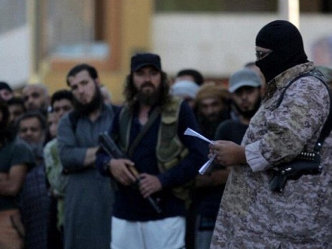 An ISIS executioner reads out charges before he brutally executes a prisoner with a sword.