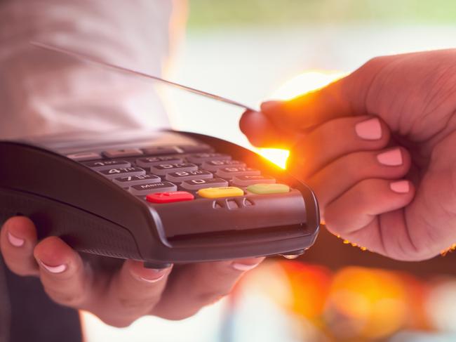 Woman paying with a credit card. She is using a contactless tapping eftpos system. Image is backlit with lens flare. Close up . Picture: iStock