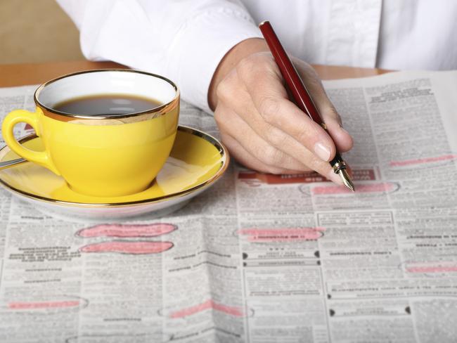 Jobs - Man with cup of coffee / tea beside him circling employment advertisements in a newspaper.