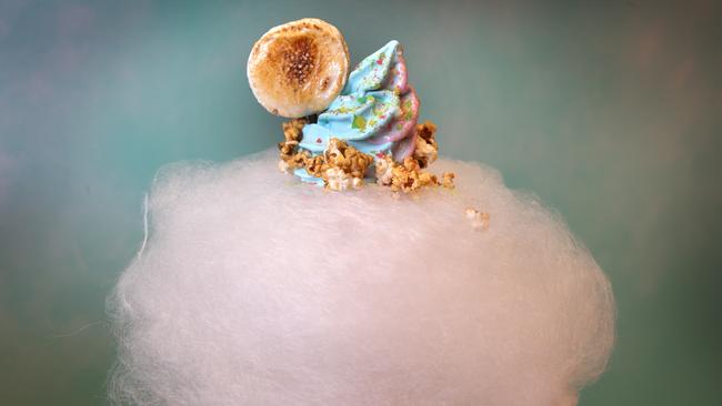 Soft serve blue ice-cream perched upon a cone topped with fairy floss, sweet popcorn, popping candy and grilled marshmallow.