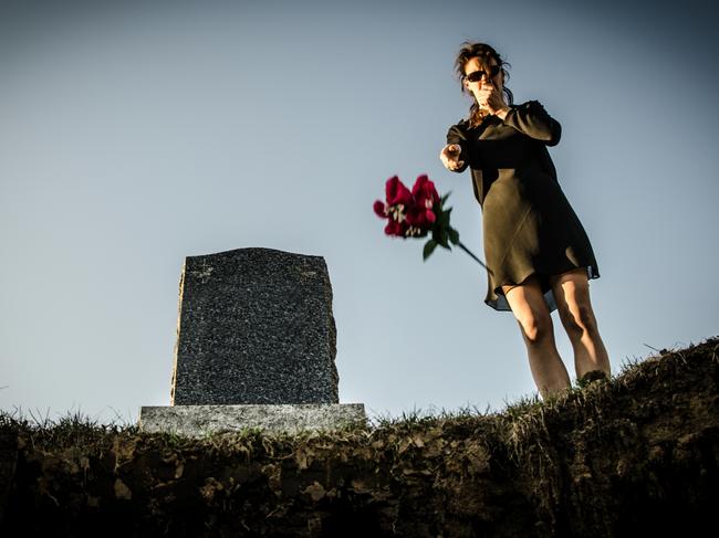 A widow cries for her dead husband in front of the hole of his fresh grave ans throws roses in the hole. Seen from inside the hole