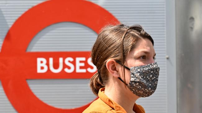 A woman wears a facemask as a preventative measure against Covid-19 as she waits at a bus stop in central London.