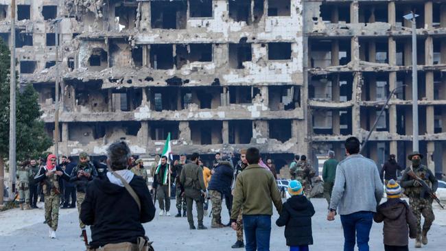 Syrian rebel fighters and civilians gather in the heart of the central city of Homs early on December 8, 2024, after rebel forces entered Syria's third city overnight. Hayat Tahrir al-Sham (HTS) and allied anti-goovernment factions have pressed a lightning offensive since November 27, sweeping swathes of the country from government control, including major cities Aleppo, Hama and Homs. (Photo by Bakr ALKASEM / AFP)