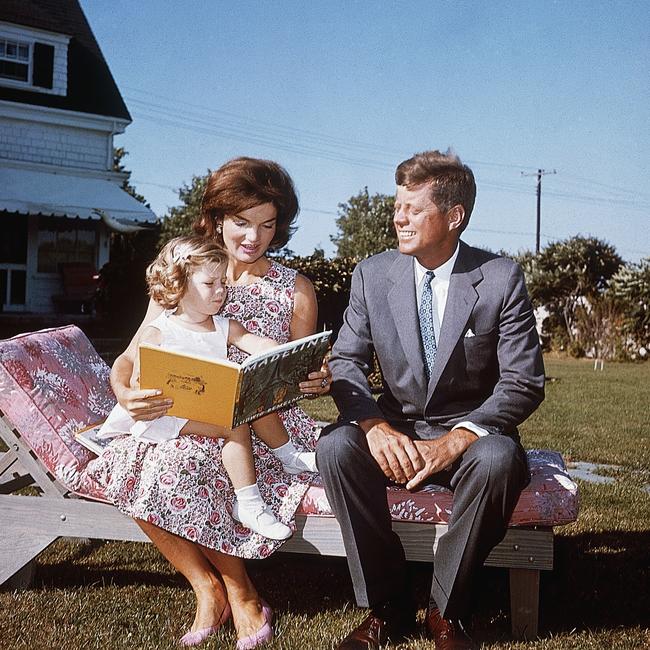 Jacqueline Kennedy and her husband John F. Kennedy sit on a lounge chair at their summer home. Jacqueline reads to her daughter Caroline from a book.