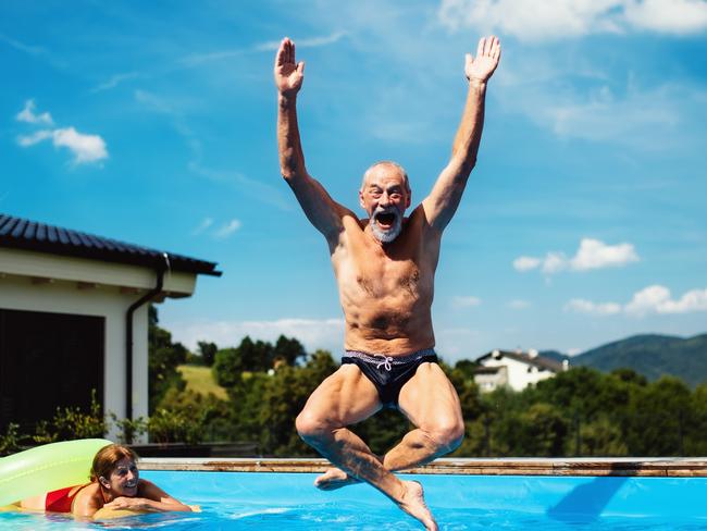 Group of cheerful seniors in swimming pool outdoors in backyard, jumping in water. happy senior, retiree generic