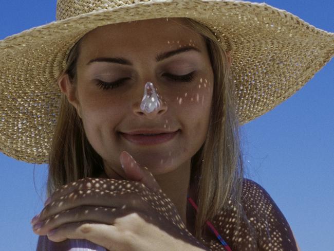 Close-up of a young woman applying suntan lotion on her shoulder