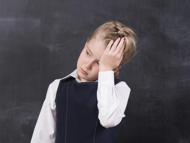 little schoolgirl with headache holding her head with hands stands at the blackboard school stress for lauren martyn jones story insight