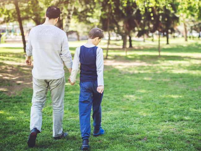 f46scope. Generic NDIS MAY 2019. Father and son holding hands and walking through park on a sunny day. Parenthood, childhood, autism awareness concept.