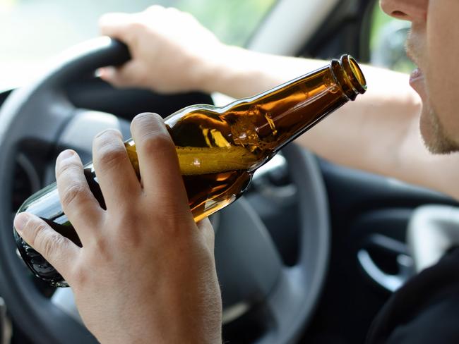 The concept of alcohol driving crime - closeup of young male driver hands with steering wheel and bottle of beer. Drink driving generic. Picture: iSTOCK