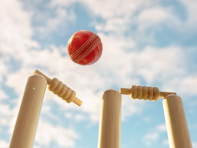 Cricket ball hitting wicket stumps knocking bails out against blue sky background