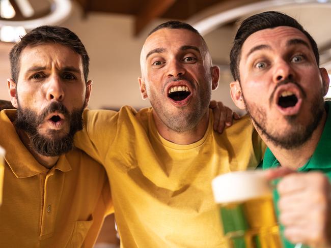 Yellow and green sports fan celebrating and drinking beer at bar