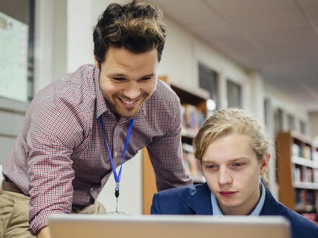 Modern teaching, teacher, technology, ipad, computers.  Teen students are working on a laptop in their school lesson. A teacher is leaning over them, helping them with some work. Picture: istock