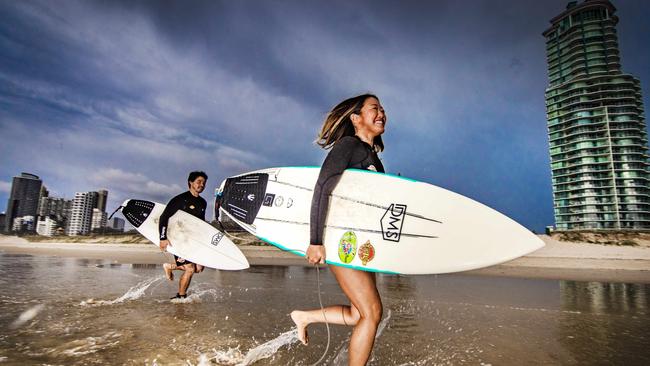 Loui Shiraseu and Sayaka Mulamatsu from Southport go for a surf a Main Beach on the Gold Coast with storm clouds overhead. Picture: NIGEL HALLETT