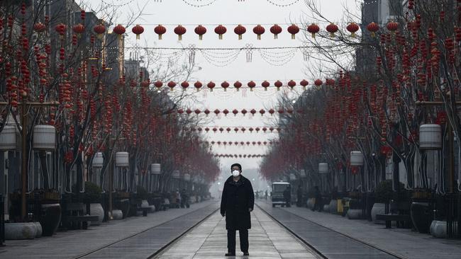 A lone pedestrian wearing a protective mask walks down an empty and shuttered commercial street in Beijing. Picture: Getty Images.