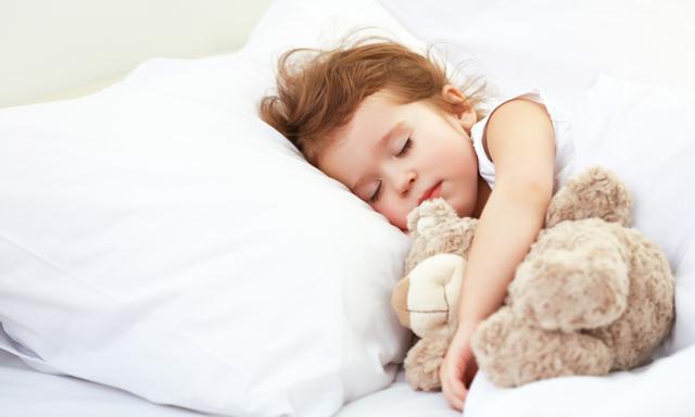 child little girl sleeps in the bed with a toy teddy bear