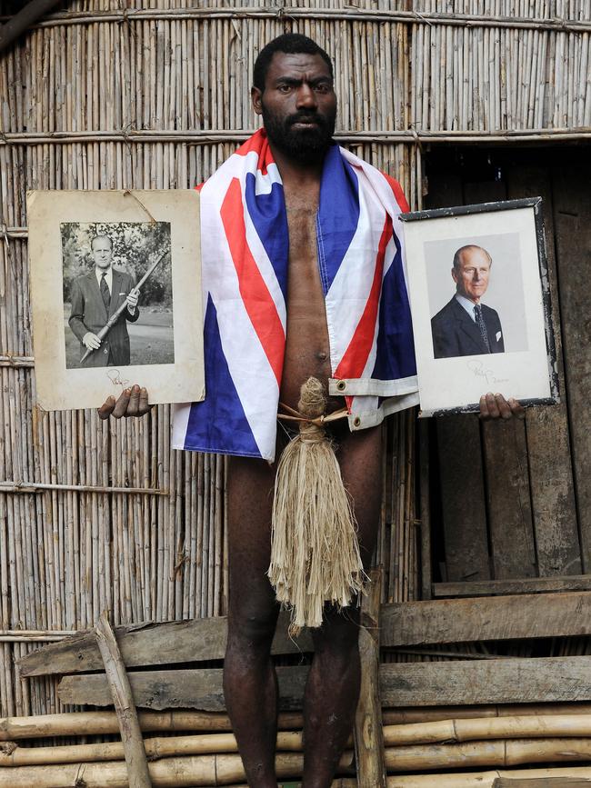 Sikor Natuan, the son of the local chief, holds two official portraits of Britain's Prince Philip in front of the chief's hut.