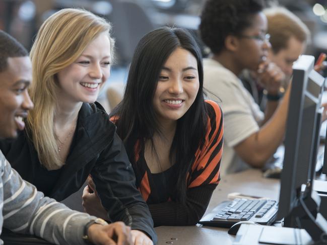 A multi-ethnic group of college age students are working together on a computer in the computer lab.