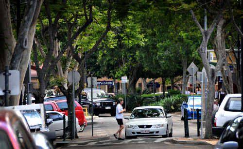 A pedestrian walks under leopard trees in Mary Street; the trees are facing the chop after their seed pods were called messy and unsafe by retailers. Picture: Craig Warhurst