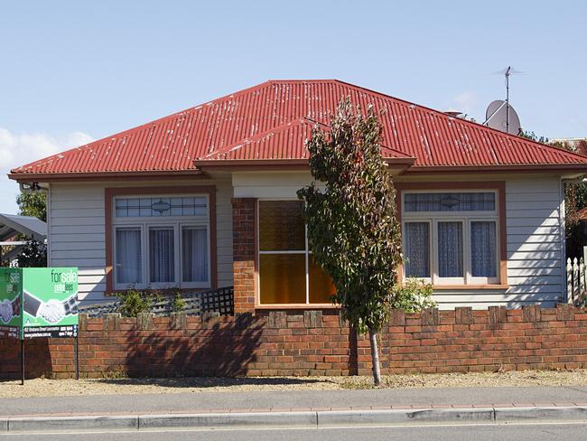 Tasmania, Australia: March 30, 2018: Street view of a typical detached bungalow in Tasmania with a red corrugated roof and a for sale sign in the garden.