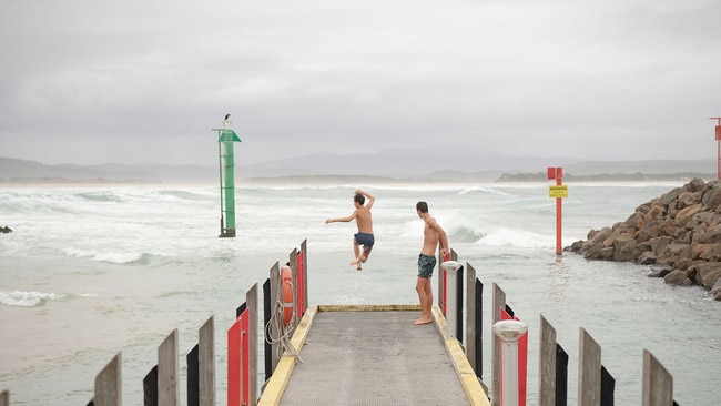 AUS MAG. Pic of 2 boys jumping off the pier where the army ships picked up residents and holiday makers from Malacoota after the fires hit on New Years day. Journo has names. They were tourists they had come back after leaving for the first time after the fires. . Pic by Nic Walker. For a story by Trent Dalton. Date 15th Feb 2020