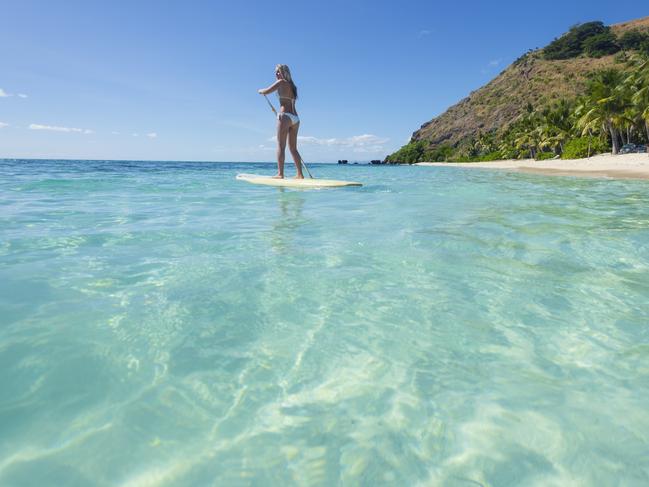 Woman paddling on a stand up paddleboard. She is wearing bikini in a tropical climate. Turquoise water in Fiji islands. Copy space