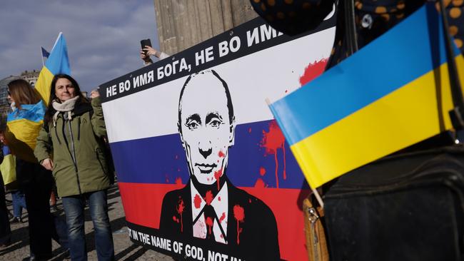 Demonstrators holding a banner showing the Russian flag and the red paint-splattered image of Russian President Vladimir Putin.