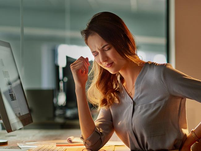 Shot of an attractive young businesswoman holding her back in pain while working late in the office