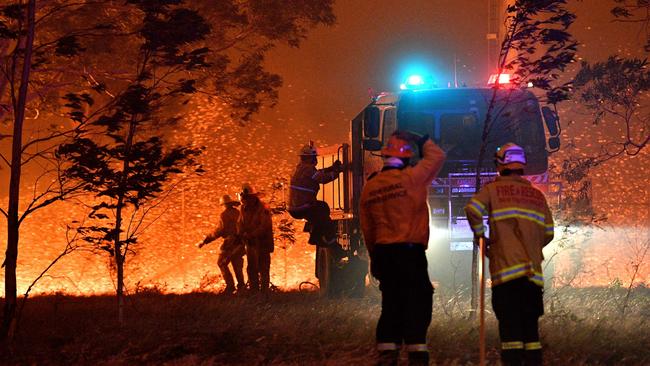 Firefighters hose down trees as they battle against bushfires around the town of Nowra in the Australian state of New South Wales on December 31, 2019. - Thousands of holidaymakers and locals were forced to flee to beaches in fire-ravaged southeast Australia on December 31, as blazes ripped through popular tourist areas leaving no escape by land. (Photo by SAEED KHAN / AFP)