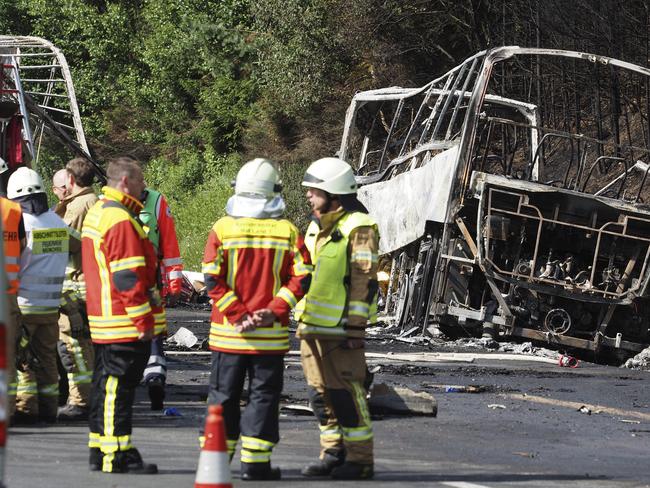 Rescue workers and fire fighters stand beside a burnt-out coach on the motorway A9.