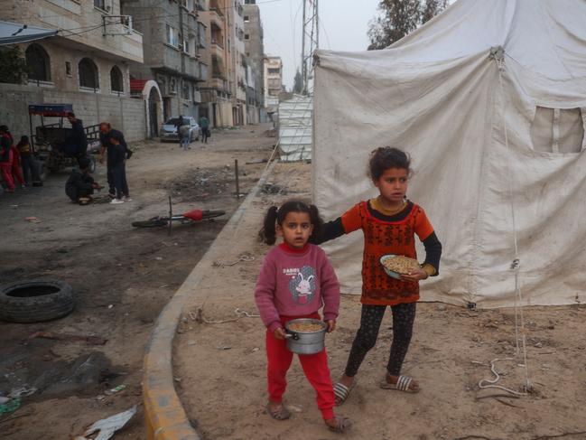 Palestinian girls carry a hot meal they collected at a charity kitchen ahead of the iftar fast-breaking meal during the Muslim holy month of Ramadan, as they walk near displacement tents at the Bureij refugee camp in the central Gaza Strip on March 5, 2025. (Photo by Eyad BABA / AFP)