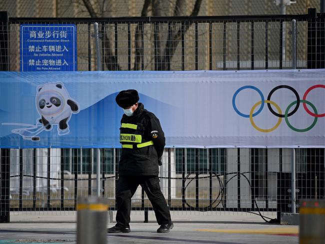 A security personnel walk in front of a picture of Bing Dwen Dwen, a mascot of the 2022 Beijing Winter Olympic Games and the Olympic Rings, at the Wukesong Sports Centre, venue for the ice hockey competition, in Beijing on January 18, 2022. (Photo by Noel Celis / AFP)