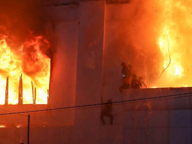 TOPSHOT - Fire burns around people on a ledge on the side of the Grand Diamond City hotel-casino in Poipet on December 29, 2022. - As many as 10 people have died in a fire at a Cambodian hotel-casino on the border of Thailand, with photos showing groups desperately huddled on ledges as fierce flames surround them. (Photo by AFP)