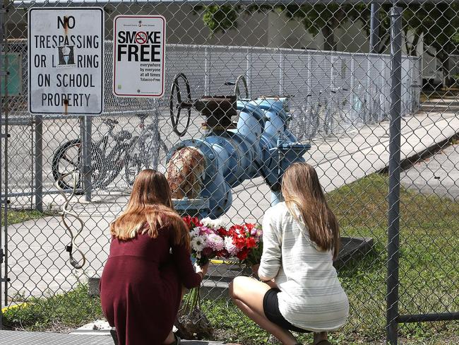 Students Jessica Garagro (l) and Sarah Goodchild, place flowers at a fence that surrounds Marjory Stoneman Douglas High School. Picture: AFP