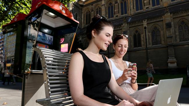 pic shows Zoe Keigtley left and Maddi Vantarakis on their phones browsing online next to theTelstra phone box in Swanston st . Telstra has rolled out free wi fi on their phone boxes across the state.