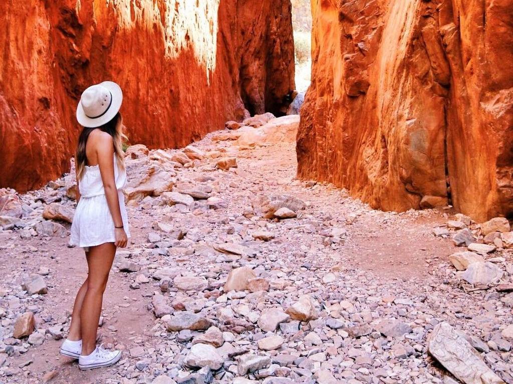 A visitor looking through the illuminated gap at Standley Chasm.Surrounded by the West MacDonnell Ranges, Standley Chasm is located in a private flora and fauna reserve. Angkerle Atwatye the Gap of Water is a striking geological formation that has significant botanical, bird-watching & wildlife photography appeal. It is an important cultural site for Western Arrernte women and now provides a backdrop for authentic cross-cultural presentations, bush tucker tours, art workshops & language classes.credit Chloe Barry Hangescapeseptember 27 2020 product