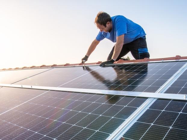 kneeling professional fixing solar panels from the top of a house roof, side view of the roof with sun reflection