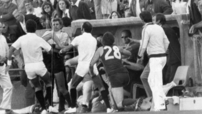 The umpires take control after Redlegs’ John Wynne crashes into the Double Blues’ dugout.