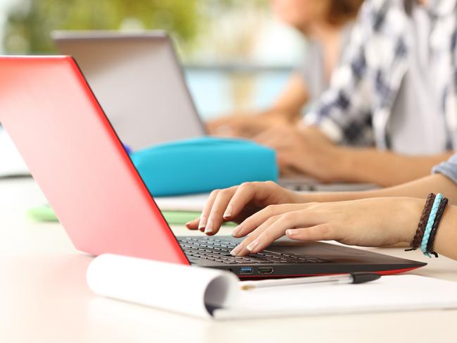 Side view close up of three student hands learning on line typing in their laptops in a classroom