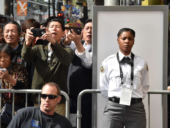 A security guard stands guard as tourists take photos of the red carpet outside the Dolby Theatre as preparations are underway for the 87th annual Academy Awards in Hollywood, California on February 21, 2015. The 87th Oscars take place on February 22 at Hollywood's Dolby Theatre. AFP PHOTO/MLADEN ANTONOV