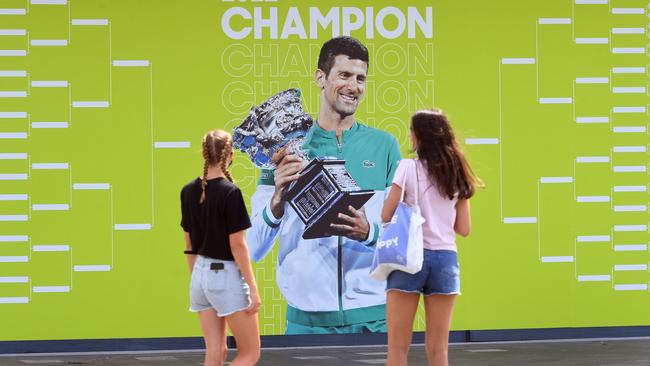 People look at an image of Novak Djokovic at the Melbourne Park tennis centre on Tuesday. Picture: William West.