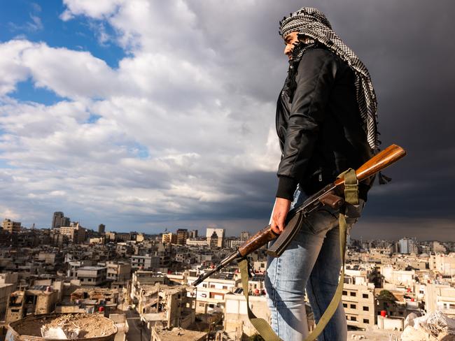 HOMS, SYRIA - JANUARY 20: A man poses with a Kalashnikov rifle while standing above the city of Homs on January 20, 2025 in Homs, Syria. Homs, the countryÃ¢â¬â¢s third-largest city, has a mixed population of Sunni and Shia Muslims, Alawites and Christians and was once called the Capital of the Revolution' and was heavily damaged in fighting over the years. Following the overthrow of Syrian leader Bashar al-Assad by opposition groups in a quick offensive on December 8, the country is looking to gain economic momentum after years of global sanctions on the Assad-led government. Arab and Western countries have been reopening diplomatic relations with Syria's new de facto authorities, headed by the Islamist former insurgent group Hayat Tahrir al-Sham, or HTS. Fourteen years of war have left the Syrian economy damaged, with tens of thousands of residents living on or below the poverty line. The World Food Program estimates that 13.1 million Syrians do not have enough to eat.   (Photo by Spencer Platt/Getty Images)