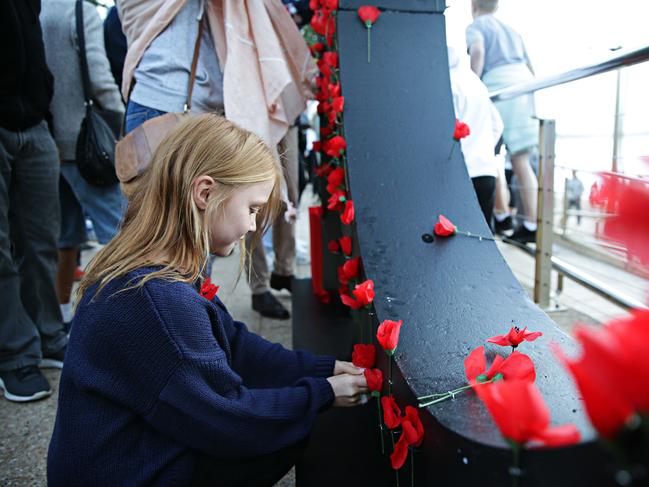 Dee Why beach Anzac Day dawn service attendees pin poppies on to a large 100 sign. Picture: Adam Yip