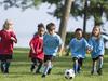 A multi-ethnic group of elementary age children are playing a soccer game outside on a sunny day at the park.