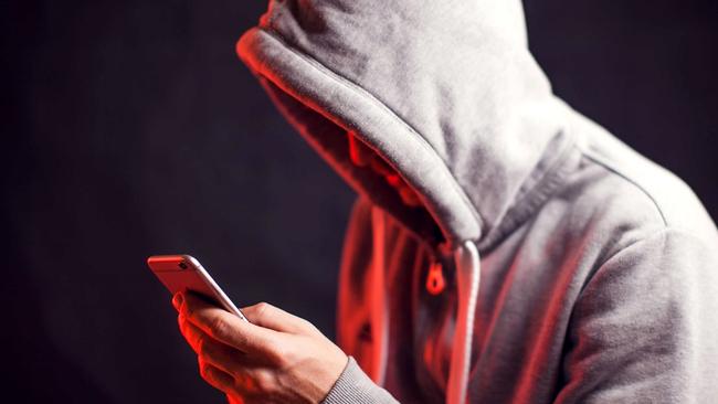 Man wearing hoody sweater with mobile phone in hands. Crime and hacking concept; scam generic.