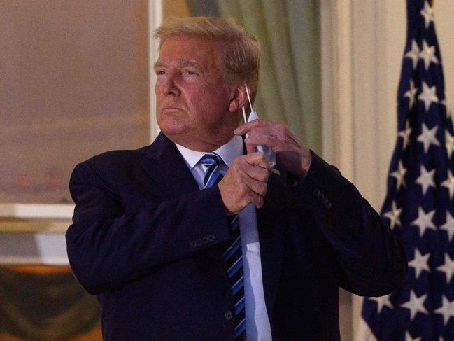 TOPSHOT - US President Donald Trump takes off his facemask as he arrives at the White House upon his return from Walter Reed Medical Center, where he underwent treatment for Covid-19, in Washington, DC, on October 5, 2020. (Photo by NICHOLAS KAMM / AFP)