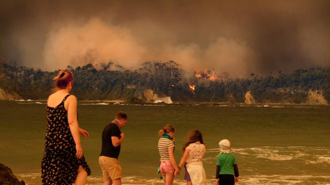 A family looks on as bushfire looms down on Malua Bay. Picture: Alex Coppel.